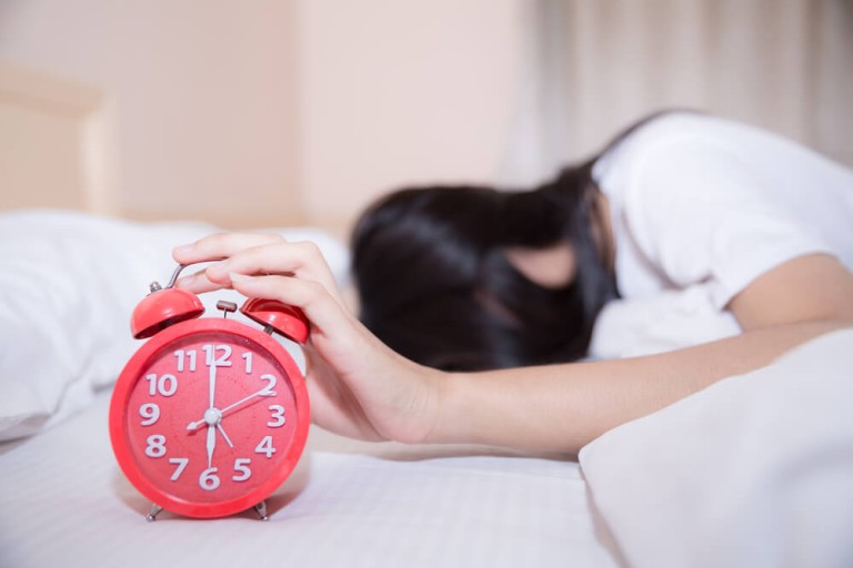הקשר בין ADHD והפרעות שינה אצל מבוגרים וילדים - אישה מנסה ל התעורר בלחיצה על שעון מעורר